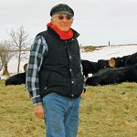 Many standing in hay-covered field with cows.