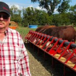 “A few years ago Dennis McMorris got tired of packing buckets of grain to feed his 350 head of cattle on his farm near Balcarres, Sask. Seaching for “that better way” he eventually developed the Bovine Bucket feeding system which has gone through extensive research and development improvements over the years. The system includes an overhead hopper on one end of the feed auger. The computerized control panel can be set so the auger delivers and drops a measured among of grain out along the feed trough on whatever timing schedule the producer wants. The unit comes in whatever length needed for any size herd. McMorris says he set up the system on his farm so he could feed four different groups of cattle with one Bovine Bucket system — feed grain or ration to a herd of pregnant cows, for example, move them out, then open a gate and bring in a group of weaned calves and so on. The Bovine Bucket was one of the exhibitors at the first-ever Ag In Motion farm show this week near Saskatoon. Along with the Bovine Bucket there were other displays of livestock handling and management equipment. The livestock component of the outdoor farm show will be expanding in future years. For more information on the Bovine Bucket visit their website at: www.bovinebucket.ca
