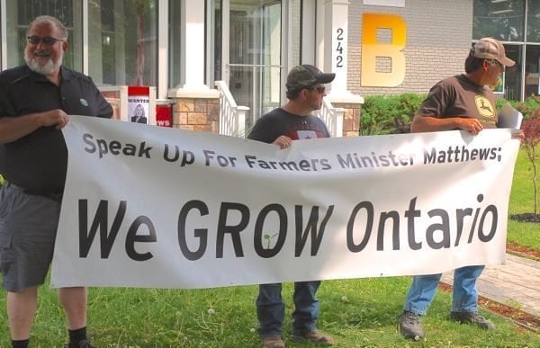 Members of Grain Farmers of Ontario sport a banner outside a provincial cabinet minister’s office in 2015. (File photo by Ralph Pearce)
