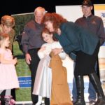 Josie Van Lent presents Rita and Armin Mueller's granddaughters with their own coveralls during a major funding announcement at Lakeland College in Vermilion. (Photo: Lisa Guenther)