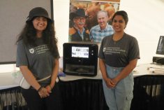 Kashika Sethi (l) and Rhea Thomas Thommana (r) were at Ag in Motion to represent food scientists Drs. Martin Reaney and Michael Nickerson and their 3D printer projects, including their work on printable protein-based materials, such as the pea-based &#8220;chicken leg&#8221; seen in the machine. (Becky Zimmer photo) 
