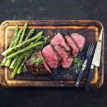 Barbecue Wagyu Point Steak with green Asparagus as close-up on burnt cutting board.