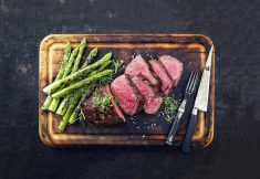 Barbecue Wagyu Point Steak with green Asparagus as close-up on burnt cutting board.