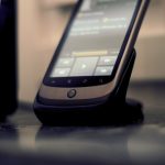 A black cellphone docked beside a computer on a desk.