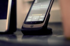 A black cellphone docked beside a computer on a desk.